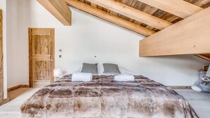 A bedroom with a wooden ceiling, a bed with a fur-like blanket, two pillows, a teddy bear, and a wooden door. - 50m from ski slopes, 5th floor, swimming pool, sauna, hammam, balcony, tv, ski locker, 93m², Tignes (Tignes)