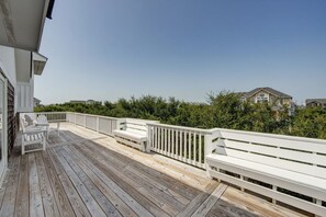 A wooden deck with white railings and benches, overlooking a residential area with houses and greenery.