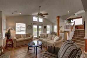 A spacious living room with a high ceiling, a ceiling fan, and a staircase leading to an upper level.