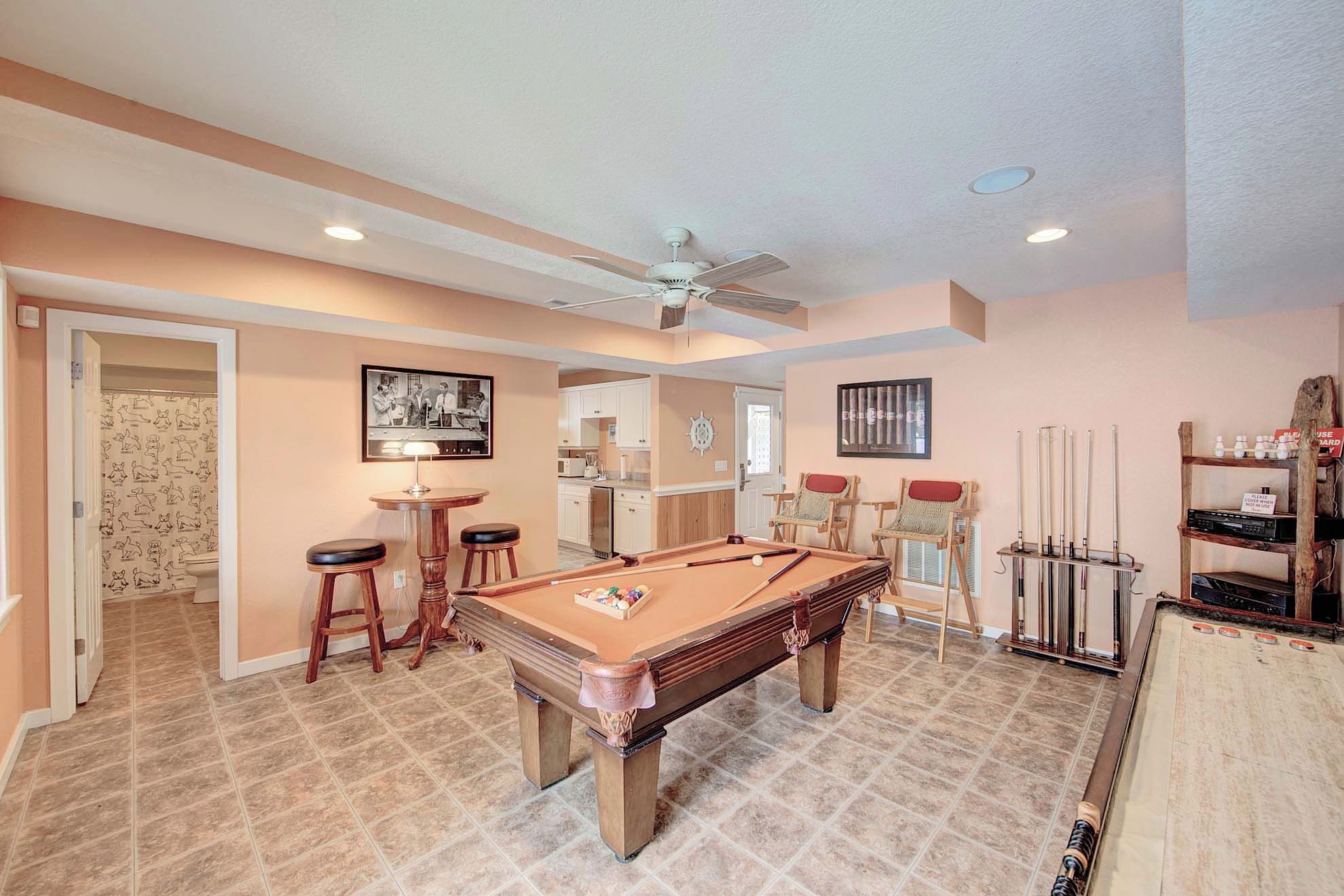 Une table de billard dans une pièce dotée d’un ventilateur de plafond, un coin bar avec des tabourets et un porte-taquets.