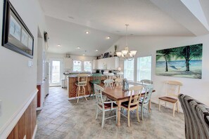 A spacious kitchen with a dining area, featuring a large island, multiple chairs, and a painting of a beach scene.