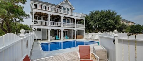 Une maison à deux étages avec une piscine, des chaises longues et une clôture blanche.
