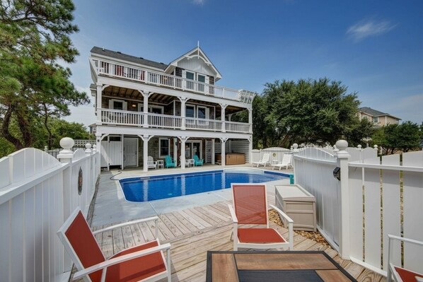 A two-story house with a swimming pool, deck chairs, and a white fence.
