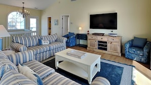 A living room with striped sofas, a coffee table, a TV, and a wooden cabinet. - Summer Wynd | Ocean Views + Community Amenities! (North Topsail Beach)
