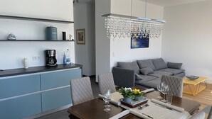 A modern living space with a dining area, a kitchen, and a grey sofa.