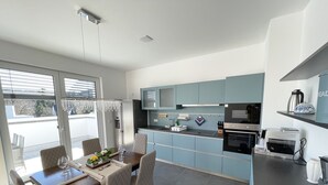 A modern kitchen with a dining area, featuring a built-in oven, microwave, and a coffee machine.