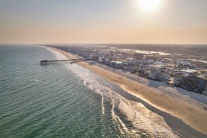 A coastal cityscape with a pier extending into the ocean, beachfront buildings, and a clear sky. - Aqua Vista: Private Pool, Steps To Beach (Murrells Inlet)