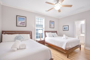 Une chambre d’hôtel avec deux lits, un ventilateur de plafond, des tableaux encadrés aux murs et une vue par la fenêtre.