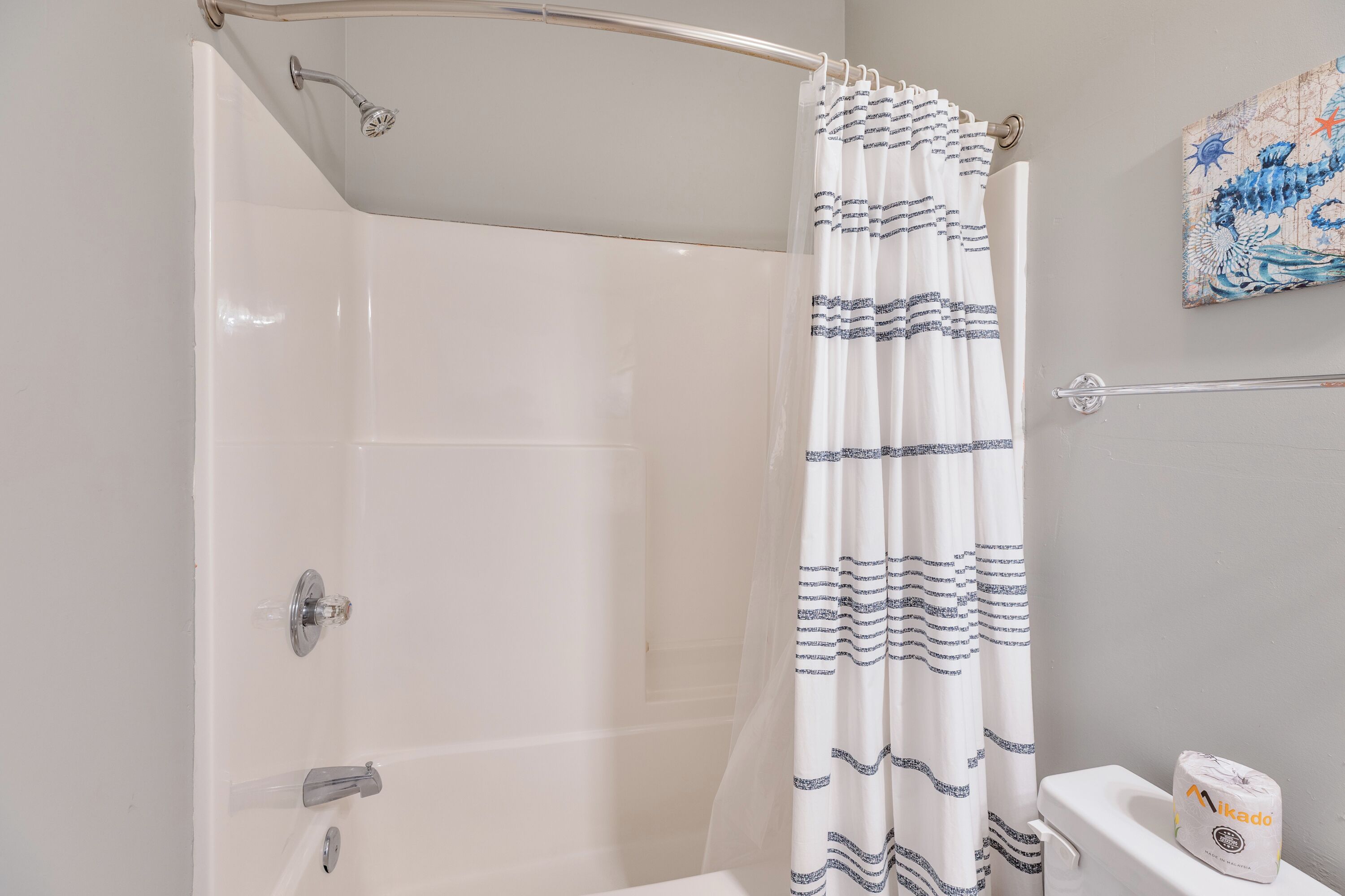 Une douche avec un rideau blanc, une porte de douche en verre et des toilettes avec un rouleau de papier toilette.