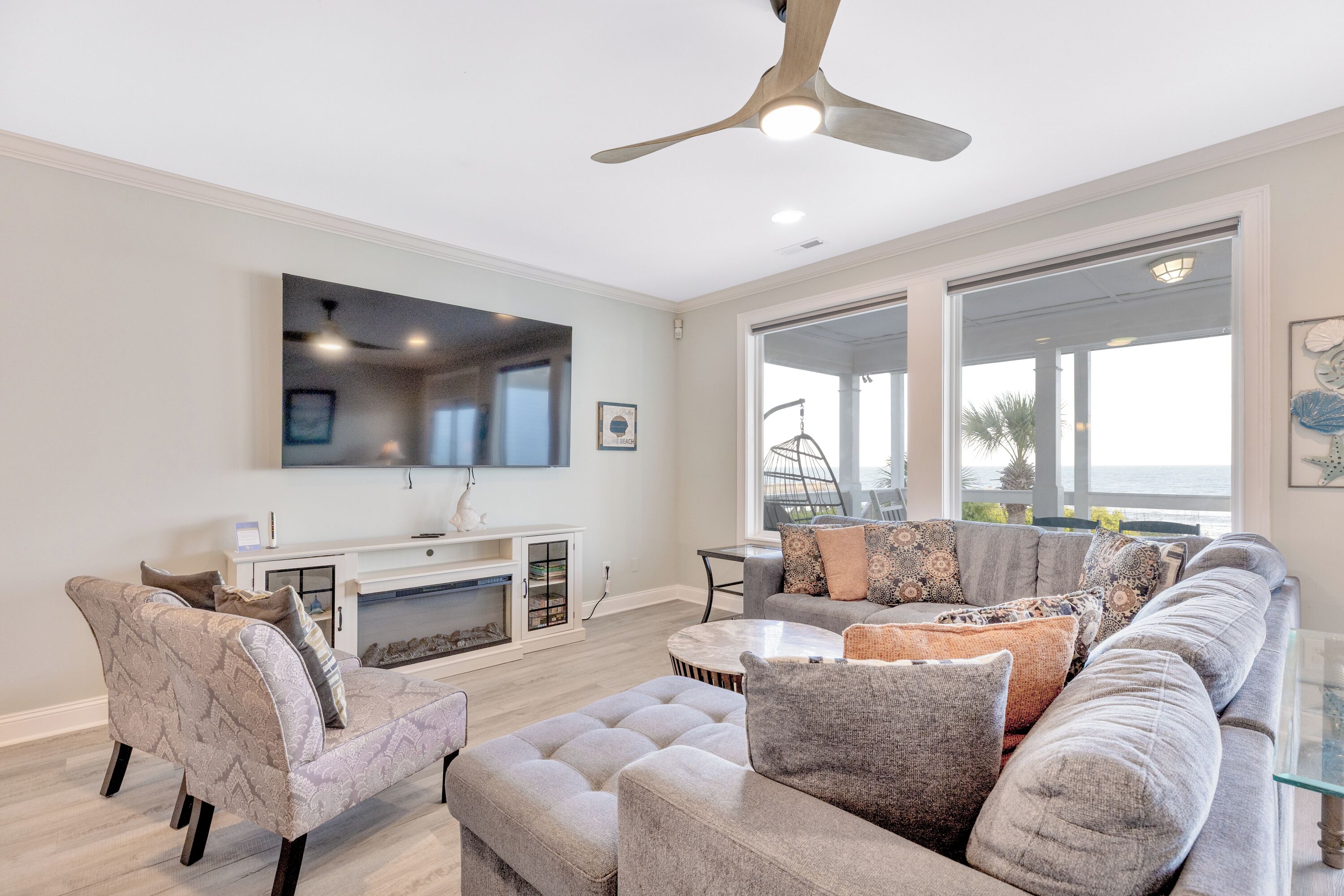 A modern living room with a sectional sofa, ottoman, and a flat-screen TV mounted on the wall.