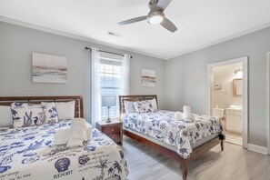A bedroom with two beds, a ceiling fan, and artwork on the walls.