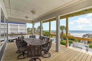 A covered outdoor area with a wooden deck, wicker furniture, and a view of the ocean. - Beach Cabana: Oceanfront + Private Pool (Surfside Beach)