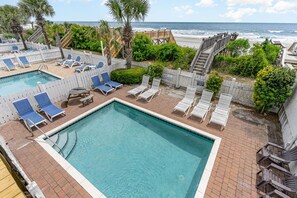 Un espace piscine avec des chaises longues et une terrasse en bois donnant sur la plage.