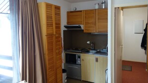 A compact kitchen with wooden cabinets, a microwave, a stove, and a sink. - Plagne Montalbert Studio 4 people (Montalbert)