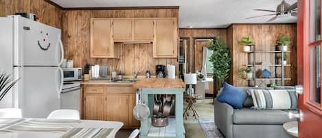 Eine moderne Küche mit Holzausstattung, ein Essbereich mit Tisch und Stühlen sowie ein Wohnbereich mit Sofa und Deckenventilator.
