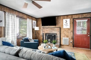 Una sala de estar con chimenea, un sofá, una mesa de centro y un televisor montado en la pared.