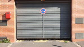 A closed garage door with a no parking sign, a red fire alarm box, and a ventilation grille on a brick wall. - Spacious apartment - Paris St Denis, stade de France (Saint-Denis)