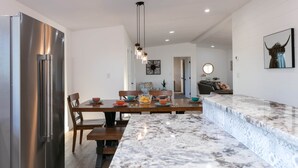 Una cocina moderna con encimera de mármol, refrigerador de acero inoxidable e iluminación colgante.