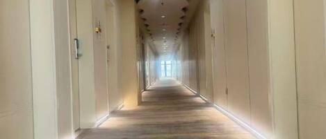 A long, narrow hallway with doors on both sides, leading to a bright end.