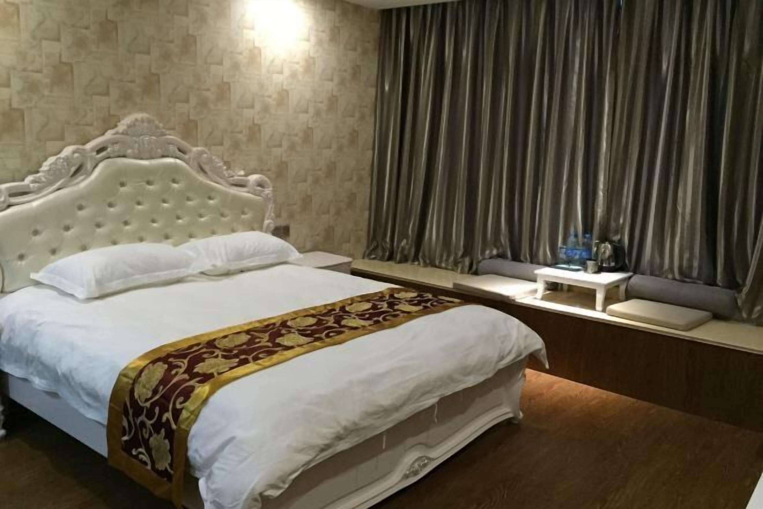 A hotel room with a large bed, a bedside table, a small table with a lamp, and a window with curtains.
