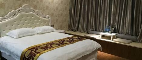 A hotel room with a large bed, a bedside table, a small table with a lamp, and a window with curtains.