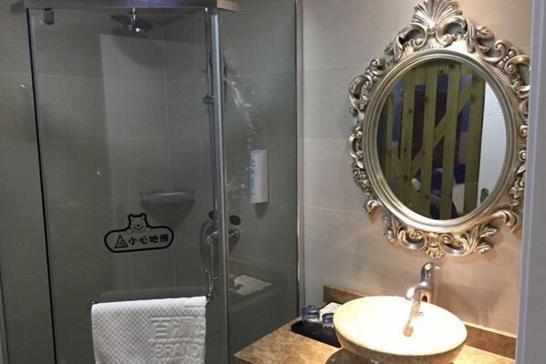 A bathroom with a glass shower enclosure, a sink with a marble countertop, and an ornate mirror. - Bailandi Boutique Hotel (Kunshan)
