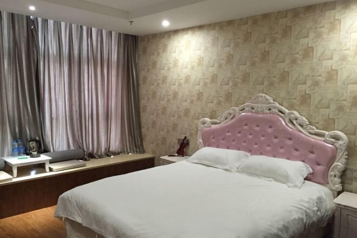 A hotel room with a bed, a nightstand, a window with curtains, and a wall with a textured pattern.