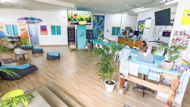 A spacious room with a wooden floor, multiple seating areas, and a reception desk with informational posters.