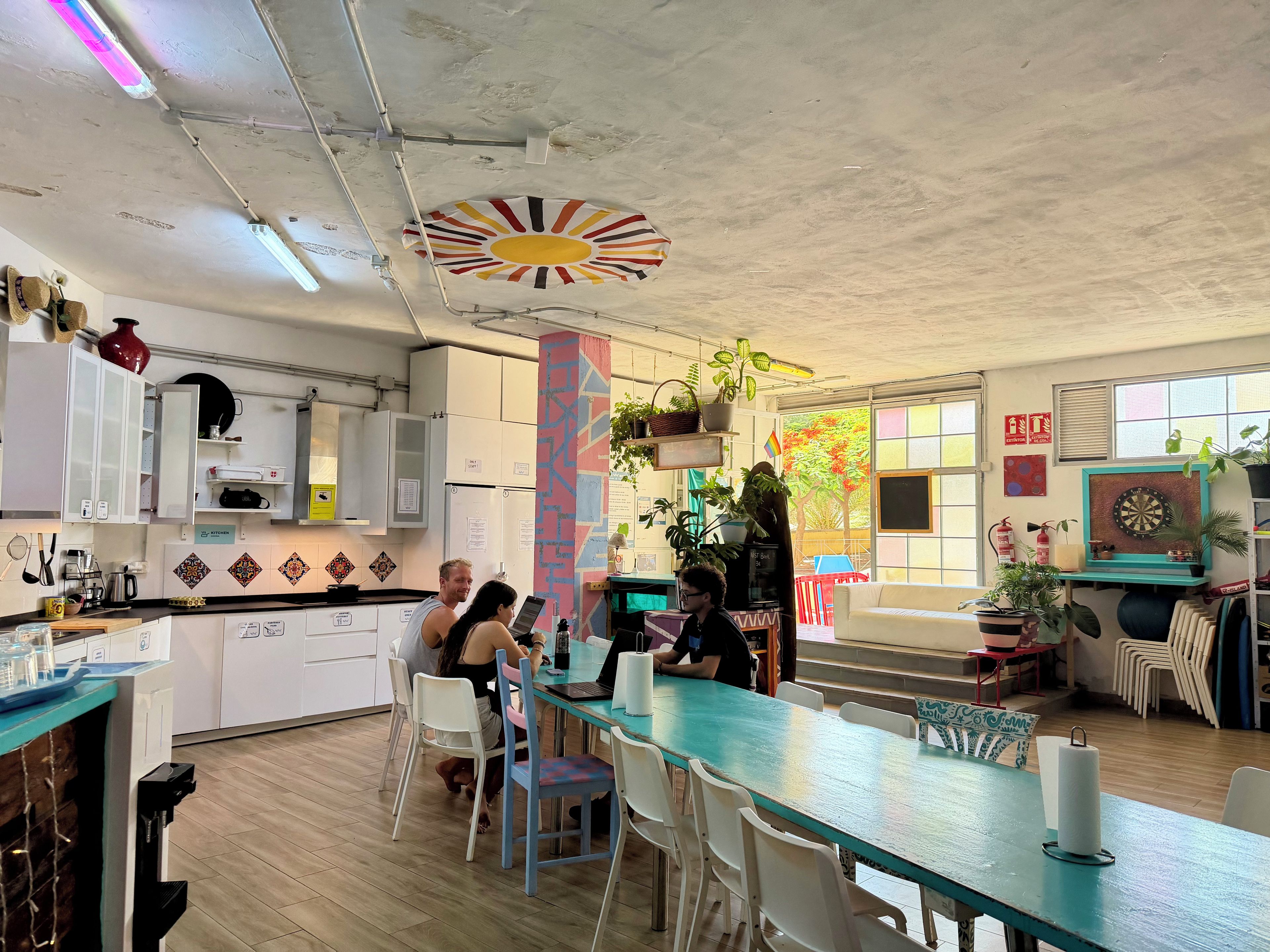 A modern kitchen with white cabinets, a teal dining table, and a colorful ceiling design.