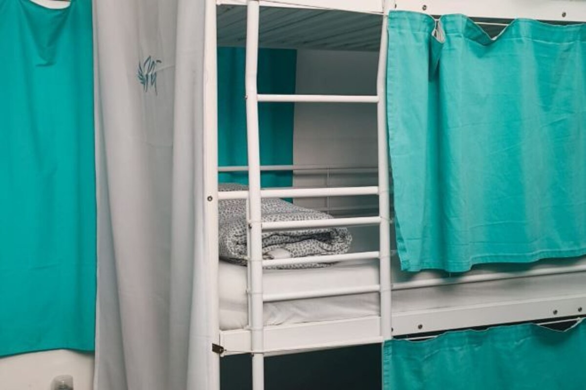 Un lit superposé avec des rideaux turquoise et un matelas blanc.