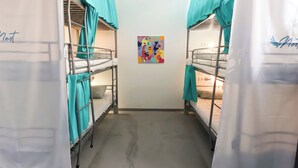 A dormitory room with bunk beds, teal curtains, a ceiling fan, and a colorful abstract painting on the wall.
