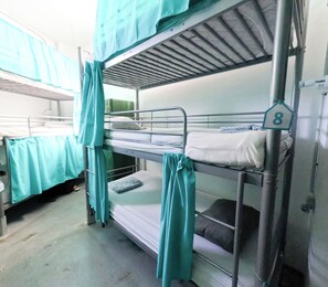 Habitación con literas, un cartel con un número en la pared, baranda de metal y una cortina.