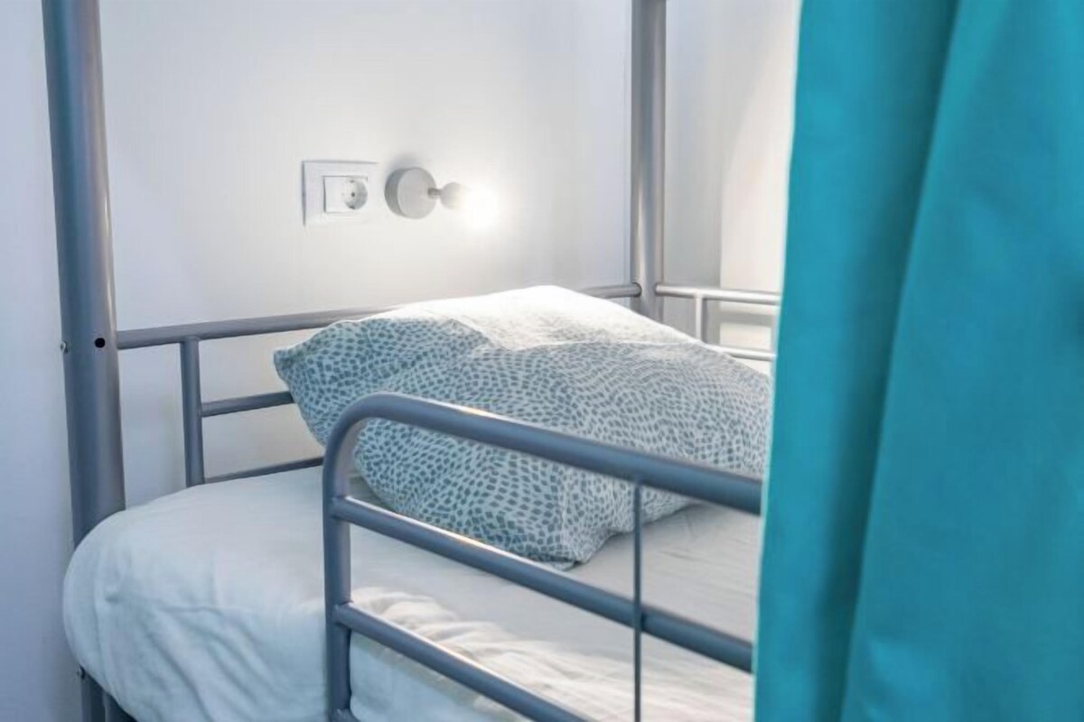 Una cama individual con estructura metálica, colchón blanco y almohadas estampadas.