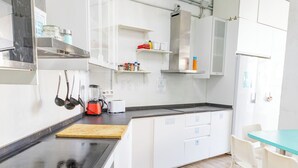 A modern kitchen with white cabinets, a black countertop, and a wooden cutting board. There is a sink, a toaster, and various kitchen utensils.