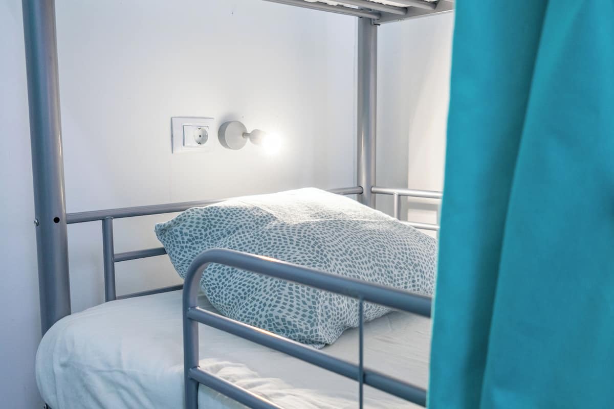 Una cama litera con un cojín estampado y una manta blanca.