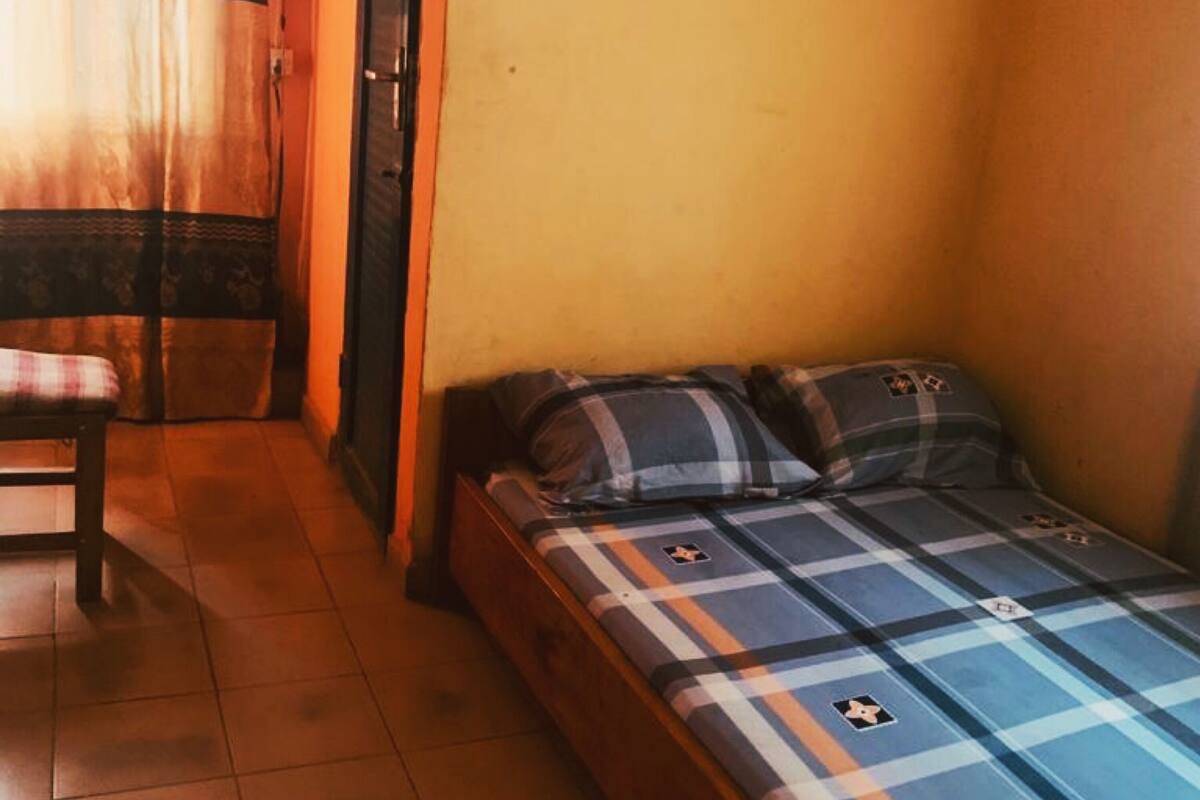 A small, single-bed room with a checkered bedspread, a chair, and a curtain.