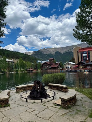 Vista de un lago con un hogar de piedra, una cabaña de madera y un edificio con techo rojo.