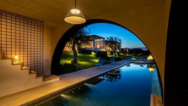 Una piscina infinita con vistas a una casa y árboles al anochecer.