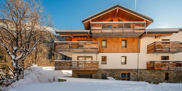 Un bâtiment en bois à plusieurs étages, doté de balcons et d’une fondation en pierre, avec un ciel dégagé.