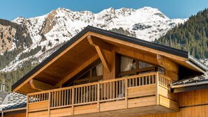 Un chalet en bois doté d’un balcon donnant sur une chaîne de montagnes enneigées.