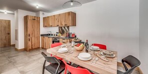 Een moderne keuken met houten kastjes, een inbouwoven en een eethoek met een houten tafel en rode stoelen.