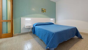 A bedroom with a bed, a nightstand, a wall-mounted shelf, a painting, and a door with a curtain. - 2242 Residence Anna - Appartamento Salmone (Taviano)