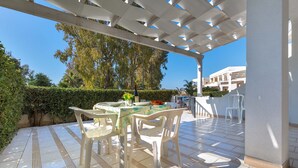 An outdoor patio area with a pergola, a table with chairs, and a view of a building in the background. - 2242 Residence Anna - Appartamento Salmone (Taviano)