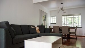 Una sala de estar moderna con un sofá modular, una mesa de centro blanca y una zona de comedor con sillas y una mesa.