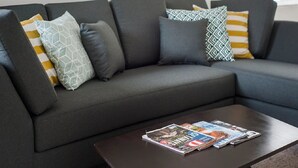 Una sala de estar moderna con un sofá seccional gris oscuro, cojines estampados y una mesa de centro con revistas.