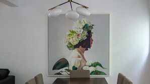 Un comedor con una mesa rectangular, cuatro sillas y un cuadro enmarcado que muestra a una mujer con un tocado floral.