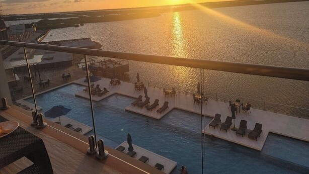 Una piscina en la azotea con zonas de solárium y vistas a la puesta de sol sobre el agua.