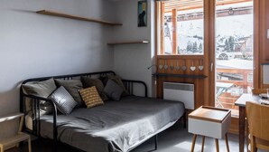 Ein modernes Schlafzimmer mit Metallbett, kleinem Schreibtisch und Fenster mit Blick auf eine verschneite Landschaft.