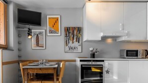 Eine moderne Küche mit weißen Schränken, einem eingebauten Ofen, einer Mikrowelle und einem Essbereich mit einem Holztisch und Stühlen.