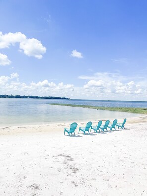 Relax on the beach with comfortable lounge chairs aligned along the shoreline, overlooking the calm waters.